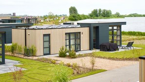 A modern building with a flat roof, large windows, and a patio area with outdoor seating. - Sustainable Holiday Home on the Ijsselmeer (Enkhuizen)