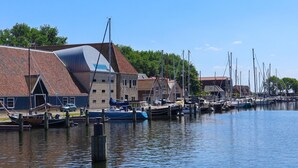 A marina with boats docked, a building with a sloped roof, and a clear sky. - Sustainable Holiday Home on the Ijsselmeer (Enkhuizen)