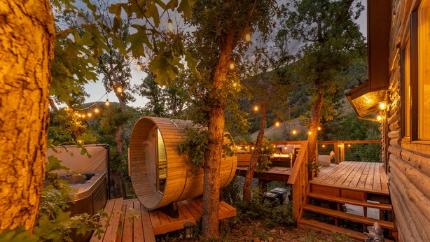 Una cabaña de madera con una habitación de forma de barril, terrazas de madera y luces colgantes.