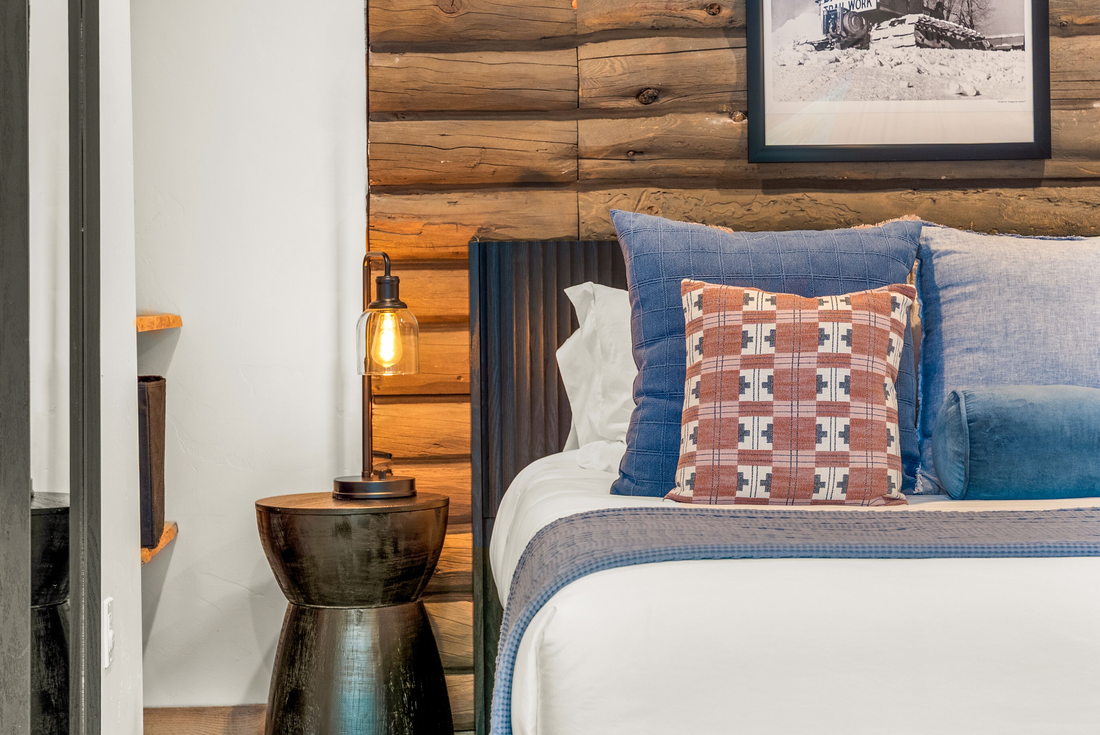 A bedroom with a wooden headboard, a bedside table with a lamp, and a bed with patterned pillows.