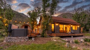 Una cabaña de troncos con terraza, asientos exteriores y luces colgantes.