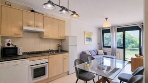 A modern kitchen with granite countertops, wooden cabinets, and a dining area with a glass table and chairs. - Serenity Apartment (Posada De Llanes)