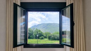 A room with a window offering a view of a green landscape and a mountain. - Serenity Apartment (Posada De Llanes)