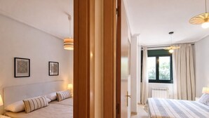 A hotel room with two beds, a window with curtains, and a radiator. - Serenity Apartment (Posada De Llanes)