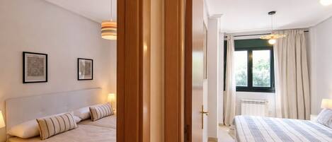 A hotel room with two beds, a window with curtains, and a radiator.