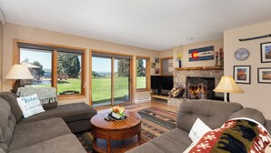 A spacious living room with a fireplace, large windows, and a cozy seating area. - Lakefront Condo, Ground Floor - Fireplace + Two Patios - Ideal for Couples or Families (Grand Lake)