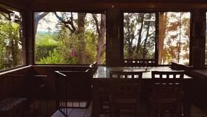 A dining area with a table and chairs, large windows with a view of greenery and trees. - Inlaquesh Villa Atitlan (Sololá)
