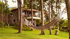 A hammock tied between trees in front of a stone building with a balcony. - Inlaquesh Villa Atitlan (Sololá)
