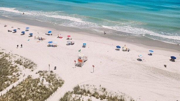 Une plage avec une eau d’un bleu limpide, un rivage sablonneux et des parasols.