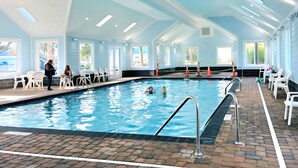 Une piscine intérieure à l’eau claire, entourée de chaises blanches et dotée d’un sol en briques.