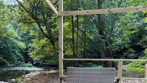 A wooden deck with wicker chairs and a table, overlooking a forested area and a body of water. - 2 Queen-Bed Canvas Bell Tent on Working Farm in Historic Laurel Highlands (Smithfield)