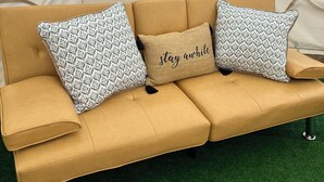 A beige sofa with patterned cushions and a 'stay awake' pillow, set on artificial green grass. - 2 Queen-Bed Canvas Bell Tent on Working Farm in Historic Laurel Highlands (Smithfield)