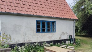 Een wit gebouw met een rood dak, een blauw raam, en een houten tafel en stoelen op de voorgrond.