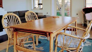 Een eetgedeelte met een houten tafel en rieten stoelen, een bank en een uitzicht door een glazen deur.
