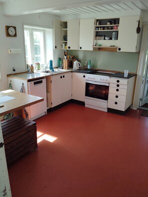A kitchen with white cabinets, a stove, a dishwasher, and a window. - Holiday cottage with a 90-degree sea view (Ærøskøbing)