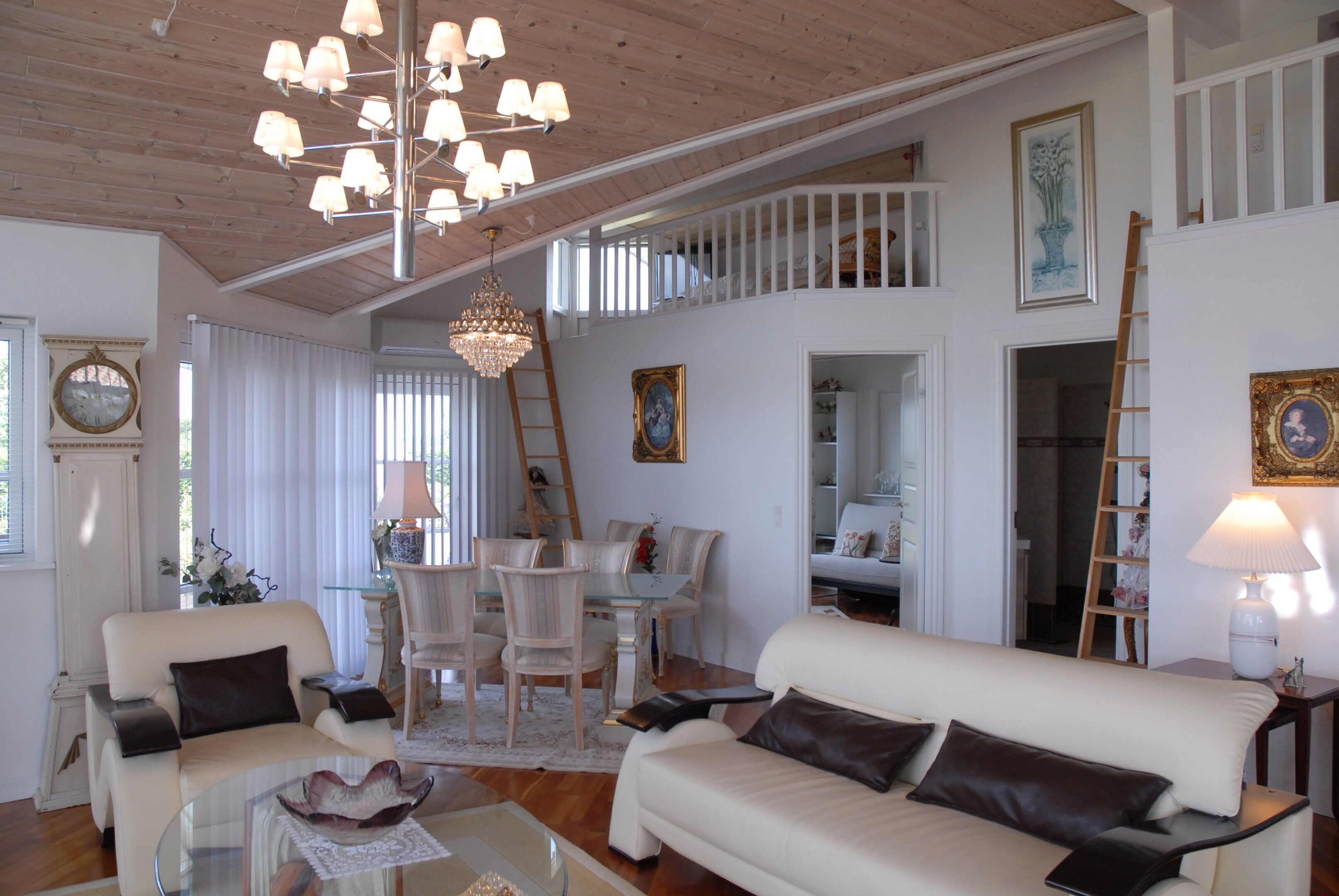 A spacious living area with a high ceiling, a dining set, and a staircase leading to an upper level.