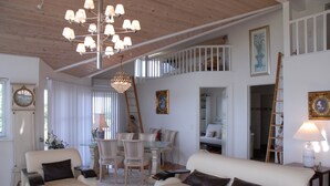 En rummelig opholdsstue med højt til loftet, et spisebord og en trappe til en etage ovenpå.