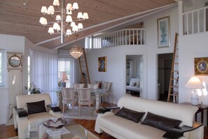 A spacious living area with a high ceiling, a dining set, and a staircase leading to an upper level.