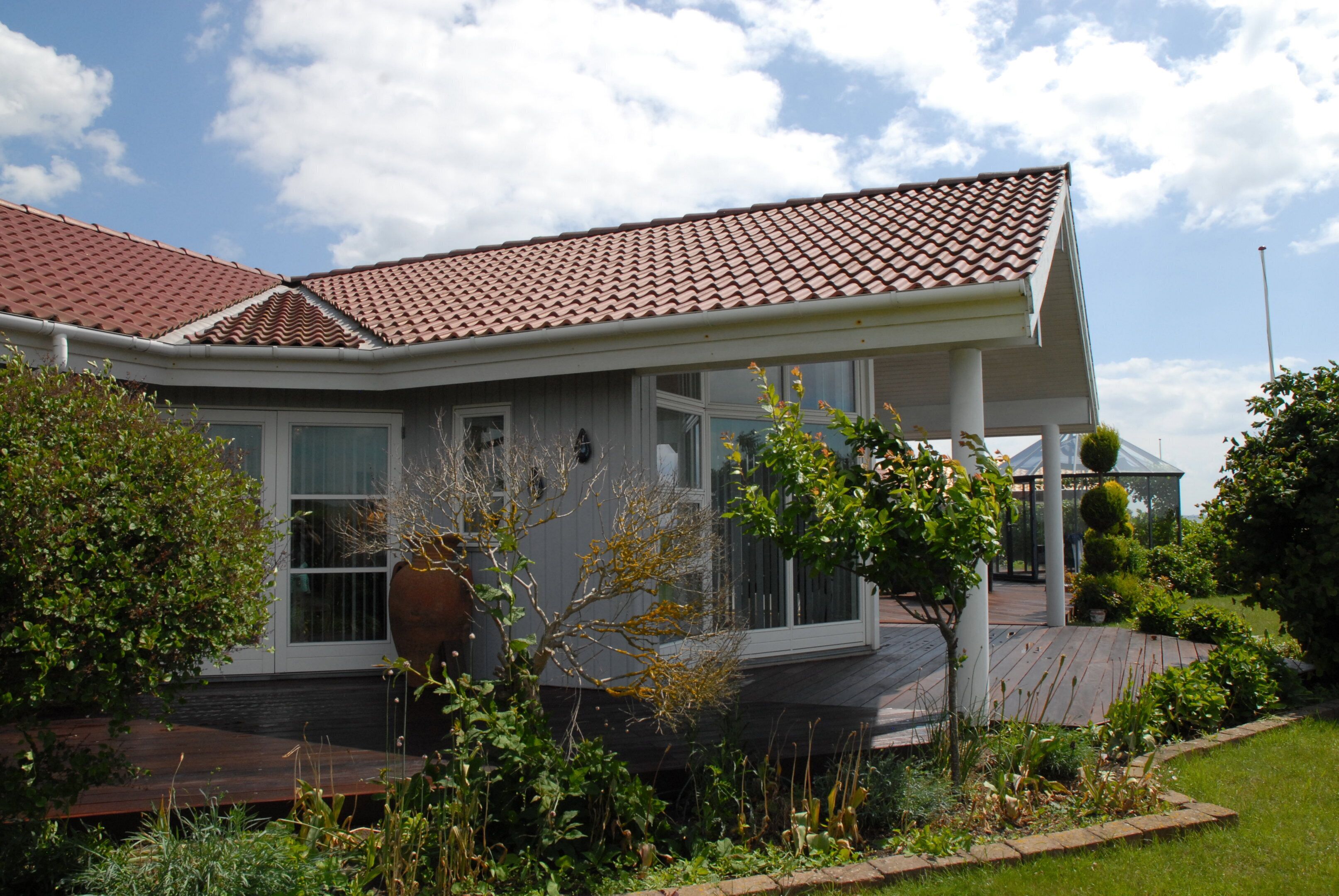 A residential house with a tiled roof, a covered porch, and a garden with various plants.