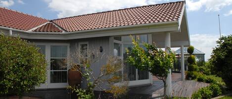 A residential house with a tiled roof, a covered porch, and a garden with various plants.