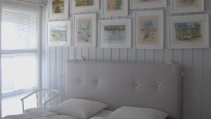 Et soveværelse med en seng, hvide vægge og billeder i rammer på væggen.