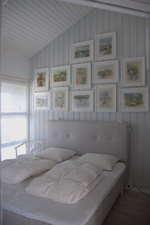 A bedroom with a bed, white walls, and framed pictures on the wall.