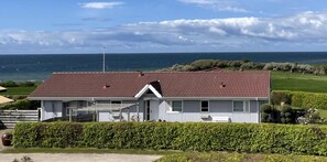 A white building with a red roof, situated near a body of water.