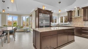 Une cuisine moderne dotée d’un grand îlot central, d’appareils électroménagers en acier inoxydable et de luminaires suspendus.