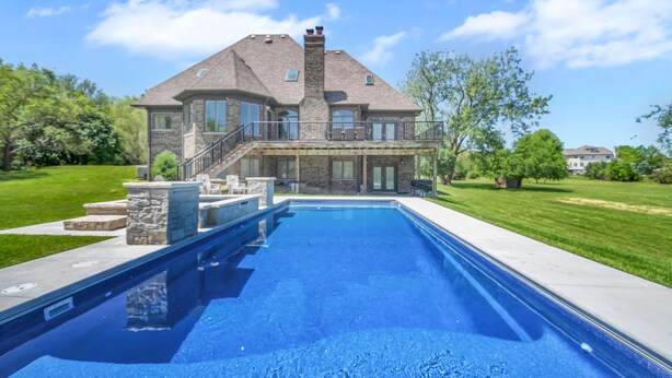 Une grande maison dotée d’une piscine, d’une façade en pierre et d’un patio couvert.