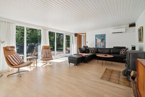 A spacious living room with a large window, a black sofa, a wooden coffee table, and a fireplace.