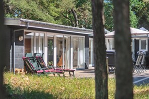 Ein Gebäude mit Glasfassade, Außenbereich mit Sitzgelegenheiten und einem überdachten Bereich mit Stühlen.