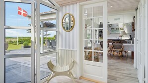 A room with a large window, a wooden ceiling, and a dining area with chairs and a table. - Fantastic summer house with sea view (Ebeltoft)