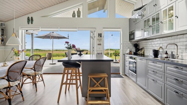 A modern kitchen with a large island, white cabinetry, and a view of the outdoors. - Fantastic summer house with sea view (Ebeltoft)