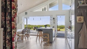 A modern kitchen with a large island, bar stools, and a view of the outdoors. - Fantastic summer house with sea view (Ebeltoft)