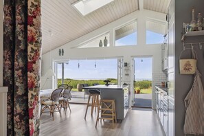 A modern kitchen with a large island, bar stools, and a view of the outdoors. - Fantastic summer house with sea view (Ebeltoft)
