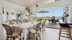 A spacious dining area with a view of the beach, white walls, and wicker chairs. - Fantastic summer house with sea view (Ebeltoft)