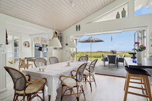 A spacious dining area with a view of the beach, white walls, and wicker chairs.