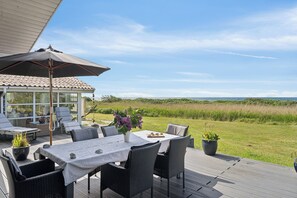 Een terras buiten met een tafel, stoelen en een grote parasol.