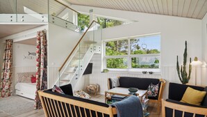 A modern interior with a staircase, a dining area, and a view of greenery outside. - Fantastic summer house with sea view (Ebeltoft)