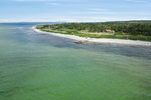 Paisaje costero con una playa, algunas casas y turbinas eólicas a lo lejos.