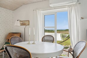 A round table with four wicker chairs, two white candles, a framed picture, and a hammock outside a window. - Fantastic summer house with sea view (Ebeltoft)