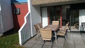 Une terrasse avec une table et des chaises, une porte-fenêtre coulissante et un mur rouge.