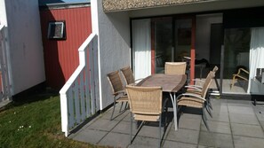 Une terrasse avec une table et des chaises, un mur rouge et une clôture blanche.