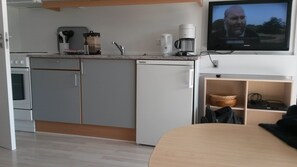 Une cuisine compacte équipée d’une machine  à café, d’un four à micro-ondes et d’un téléviseur fixé au mur.
