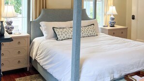 Een hemelbed met witte lakens, een kussen met een patroon en een nachtkastje met een lamp.