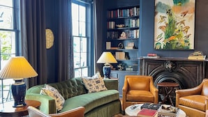 Een gezellige woonkamer met een groene bank, leren fauteuils, een open haard, een boekenkast en een groot schilderij.