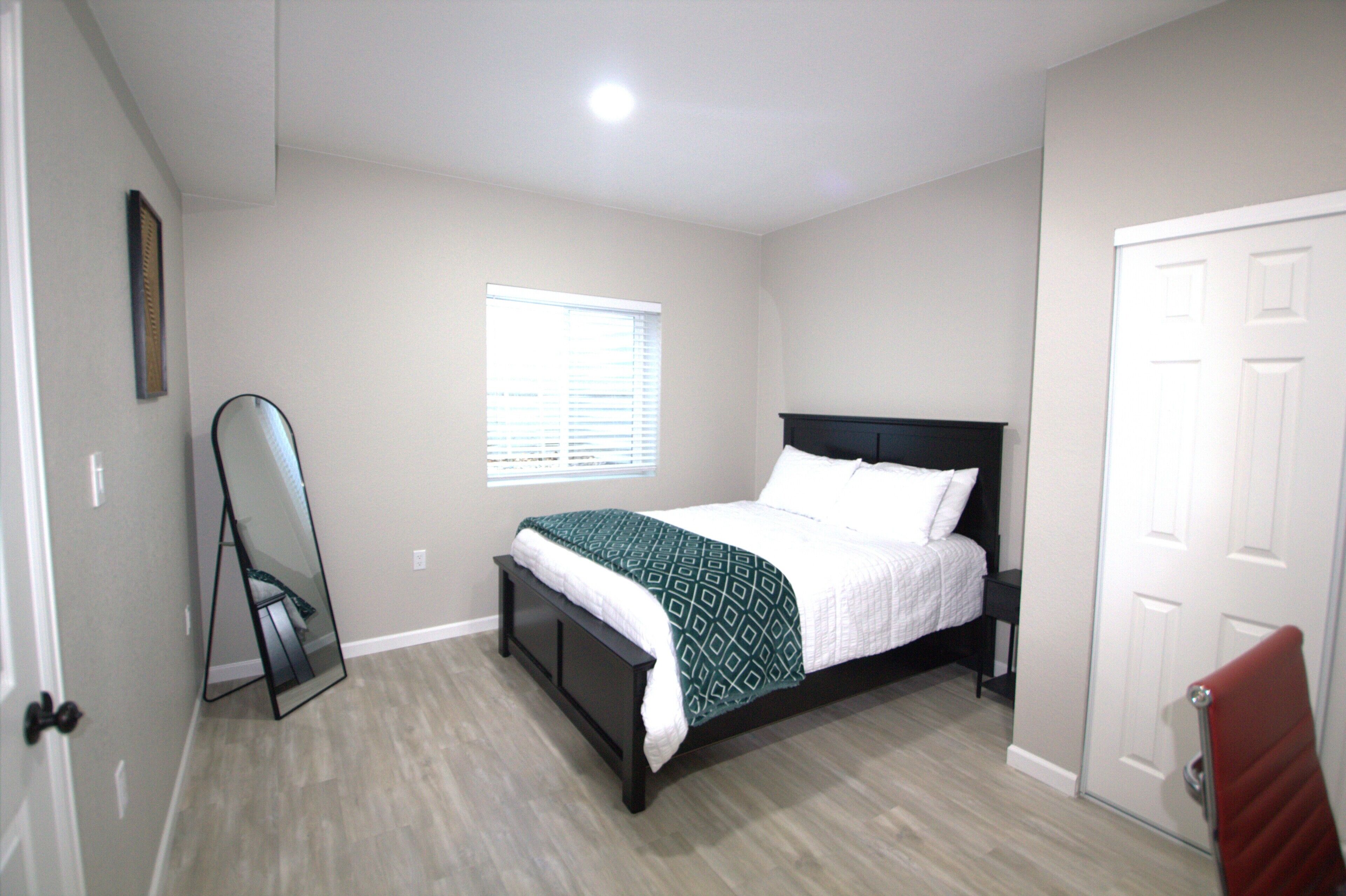 A bedroom with a bed, a window, a door, and a mirror.