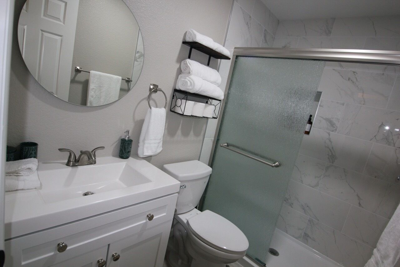 A bathroom with a white sink, mirror, and toilet. There is a glass shower enclosure and a towel rack with folded towels.