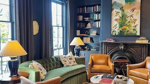 A cozy living room with a green sofa, leather armchairs, a fireplace, a bookshelf, and a large painting. - Luxury Private Suite in Boutique Historic Inn The Athenian -Downtown Location (Athens)
