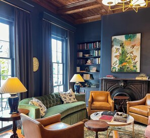 Un salon chaleureux avec un canapé vert, des fauteuils en cuir, une cheminée, une bibliothèque et un grand tableau.